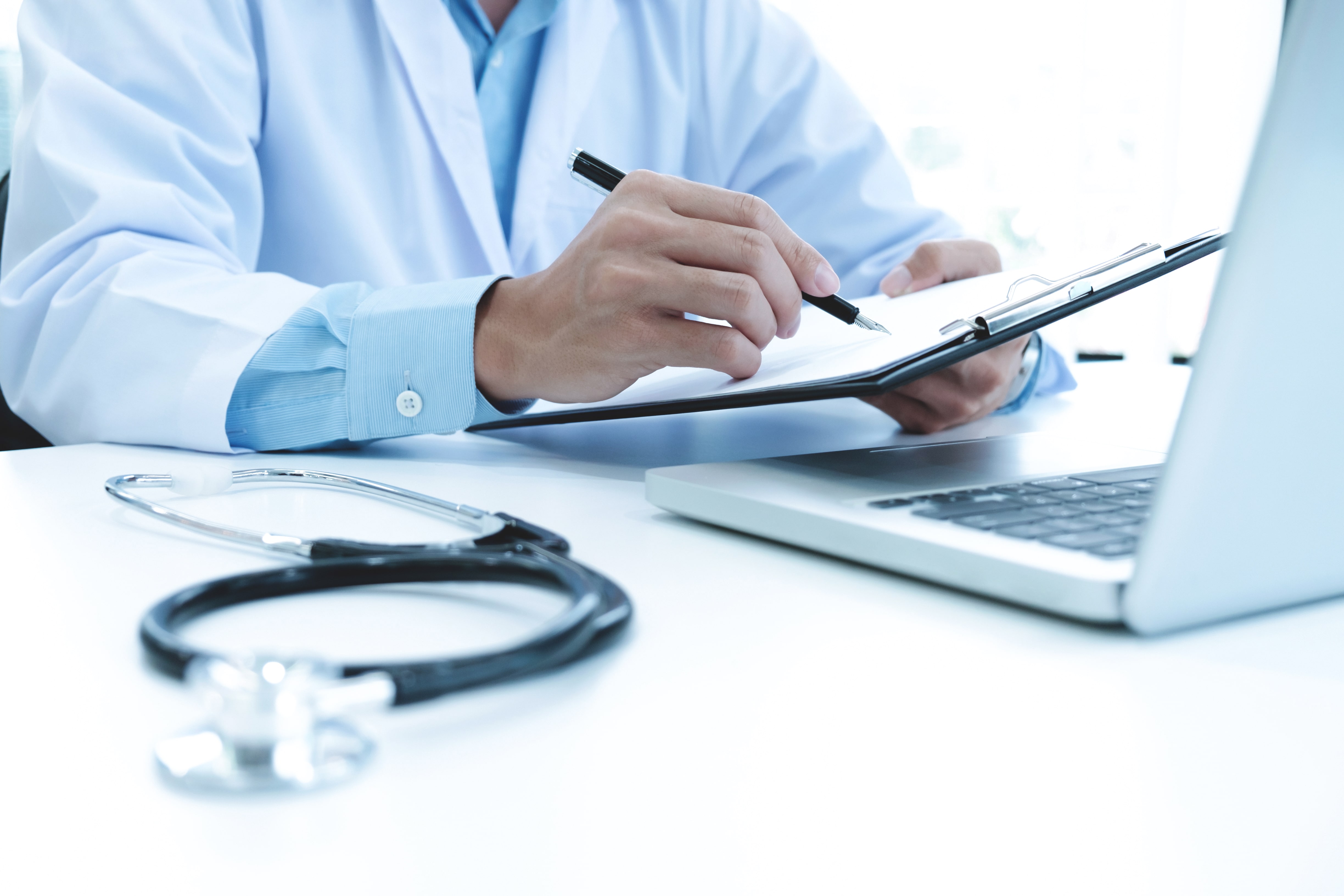 doctor-working-with-laptop-computer-writing-paperwork-hospital-background-min